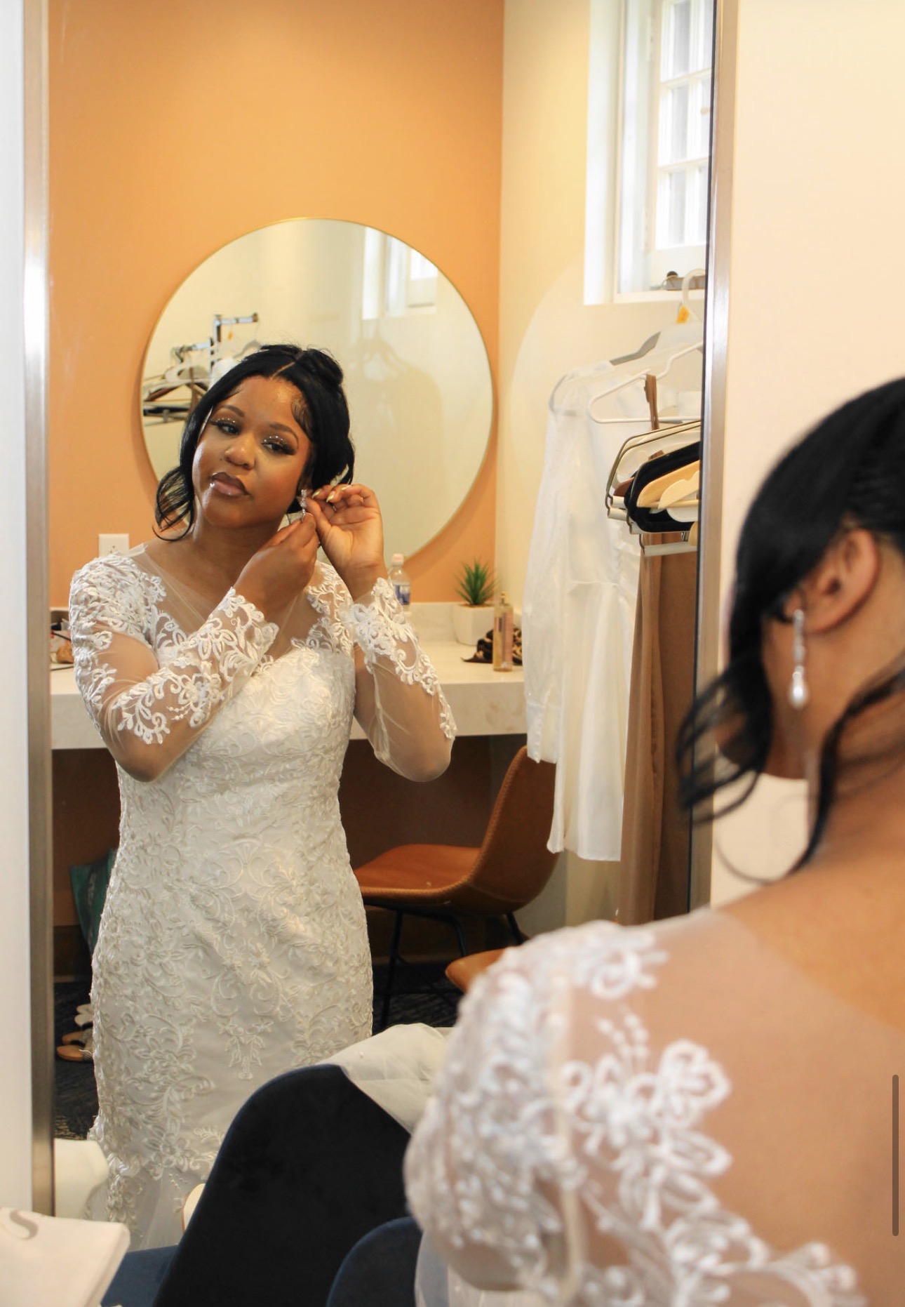 Bride fastening her earring in front of a round mirror while getting ready