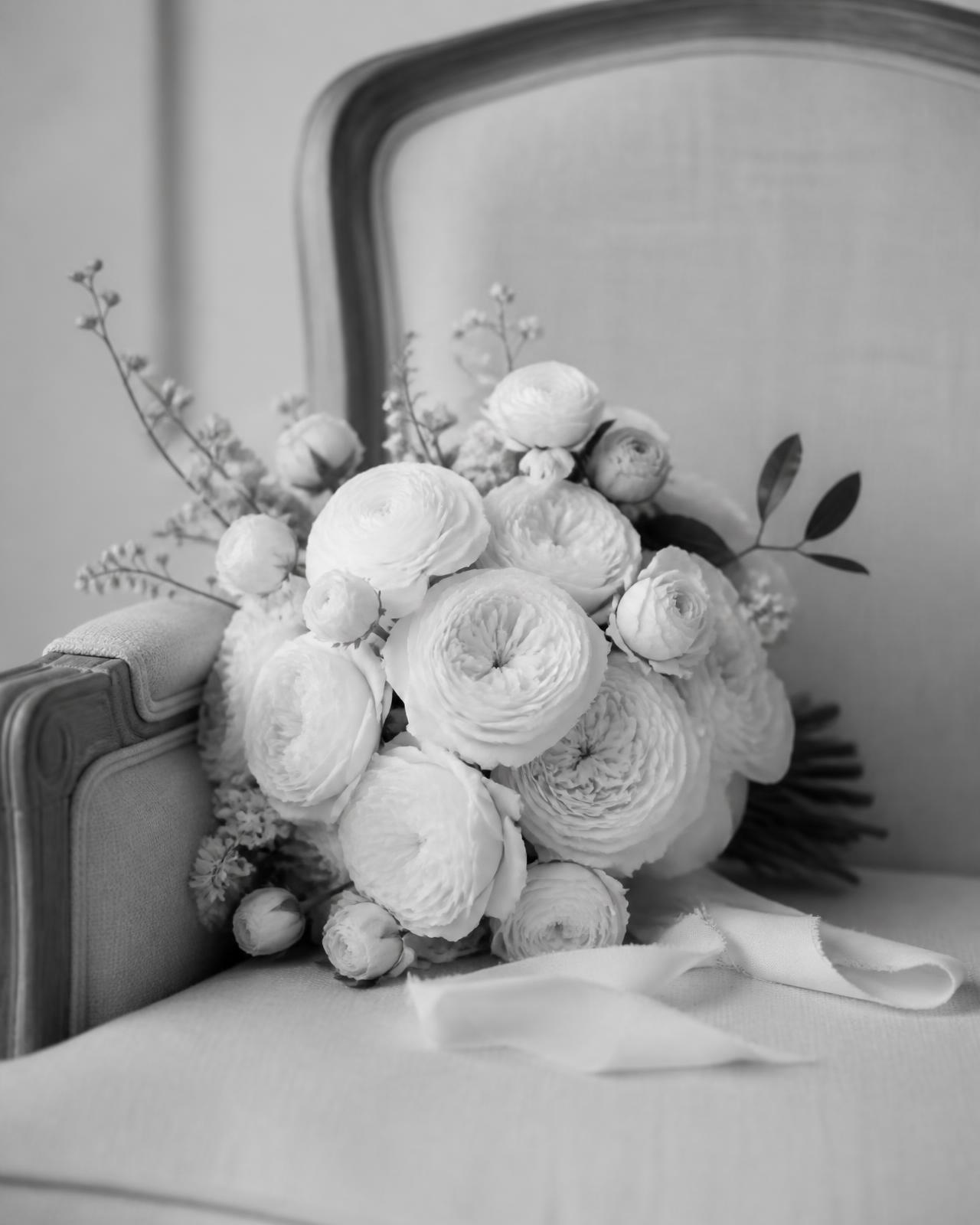 Bridal bouquet of white garden roses and ranunculus resting on a linen chair